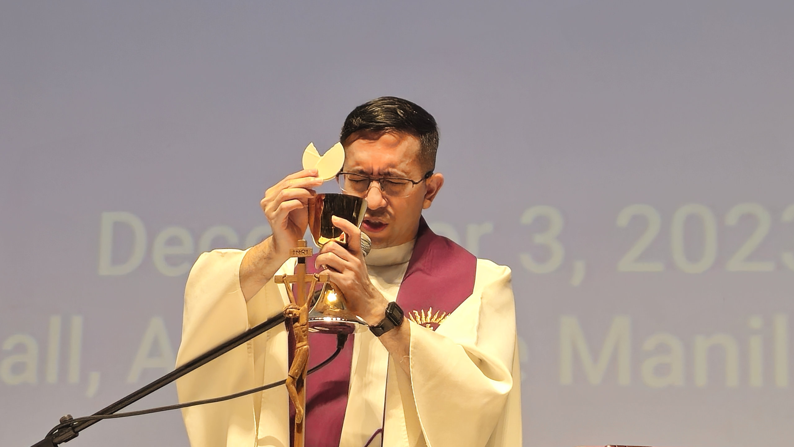 A priest holds a split host above his chalice of wine.