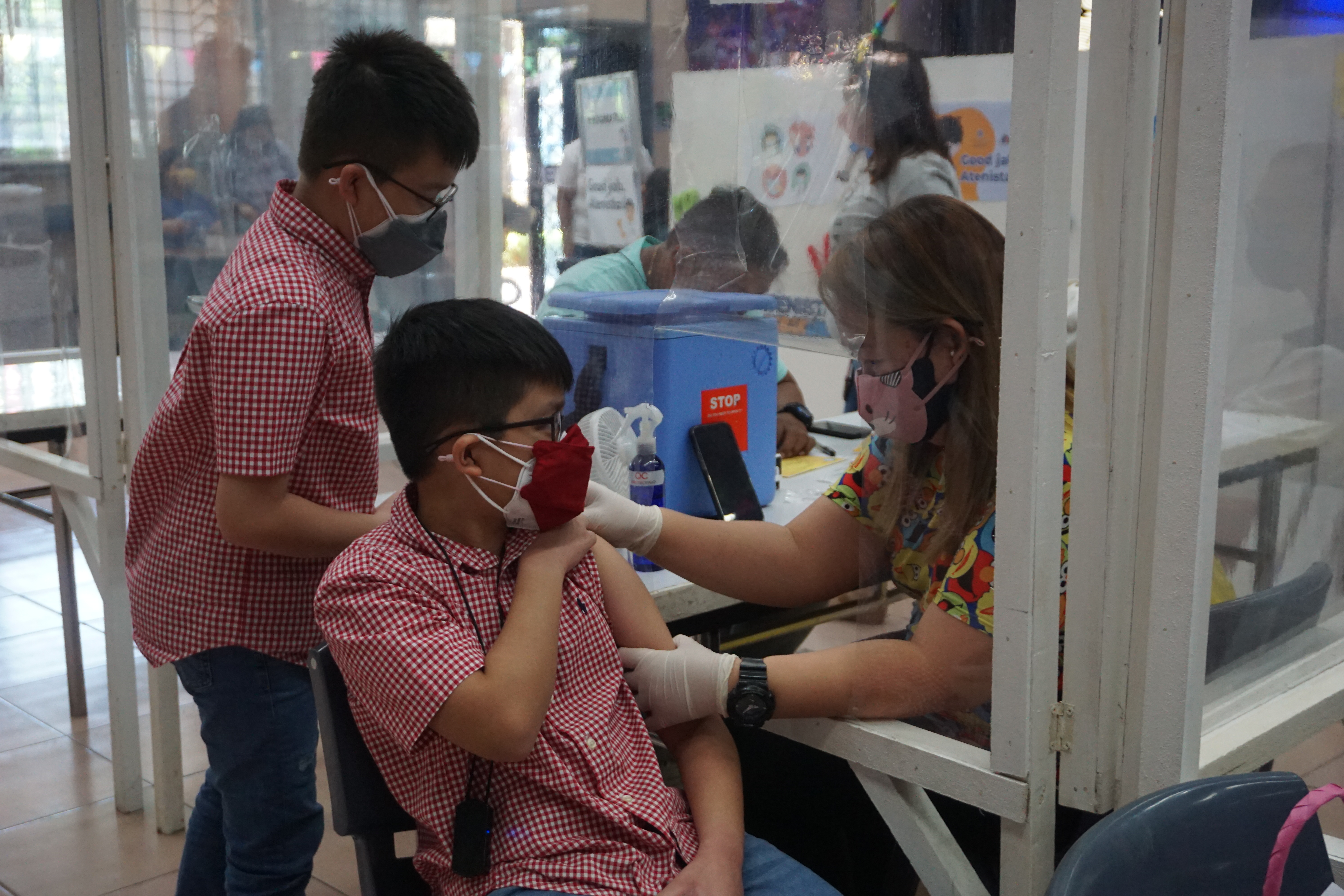 Andres Emmanuel (grade 5, standing) watches as his twin Anton Emmanuel gets the jab