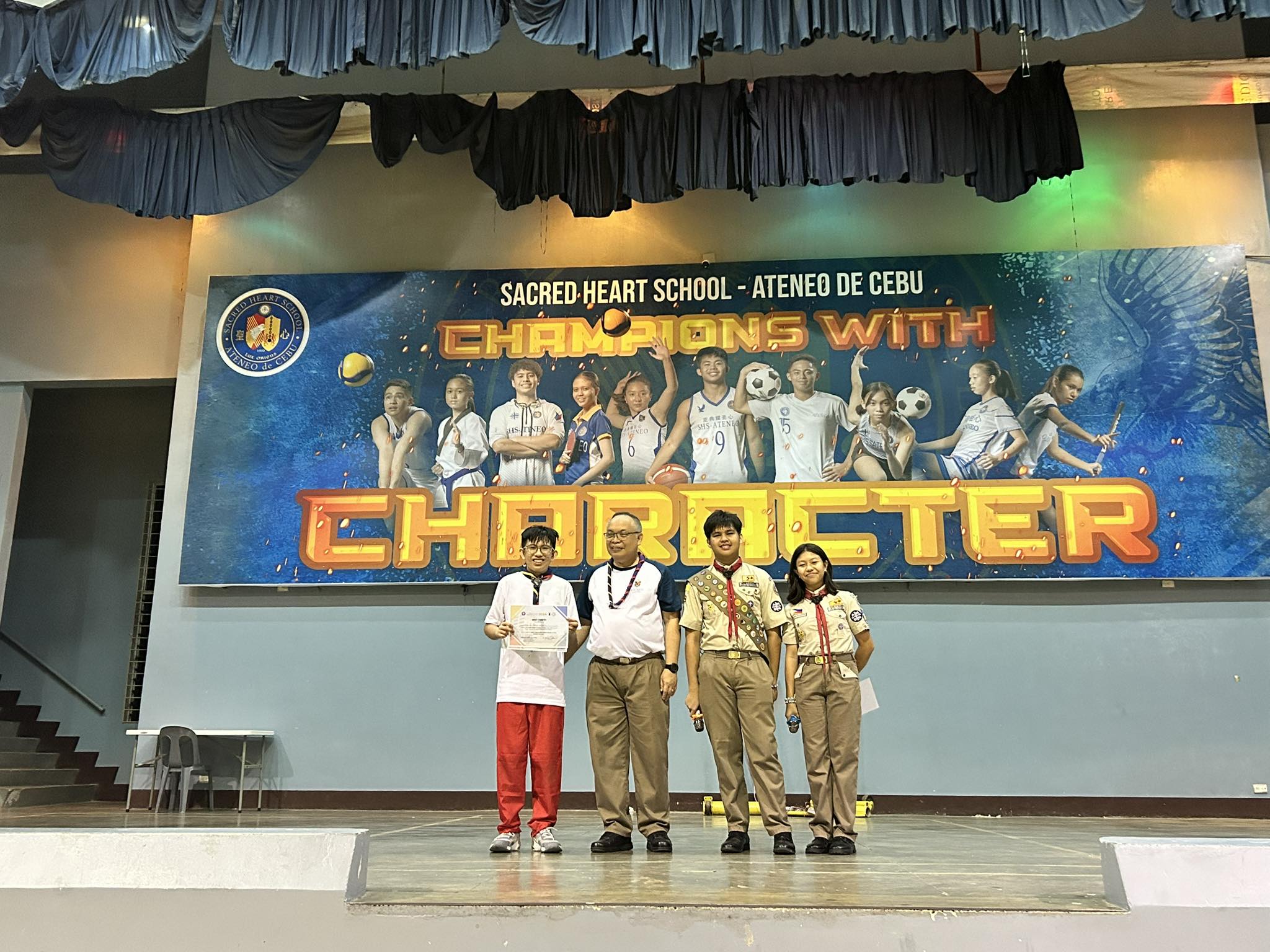 An Ateneo de Manila Senior Scout representative (left) receives the awards for “Biggest Delegation” and Most Thrifty” from Fr Jonjee Sumpaico SJ 