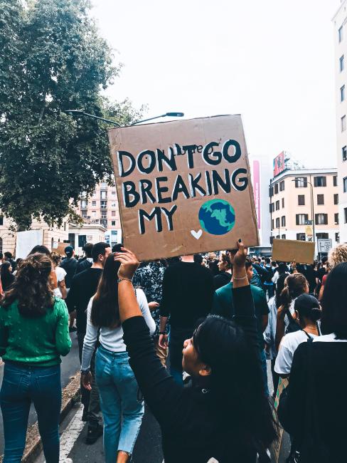 A climate protester holding a placard that reads "Don't Go Breaking My Heart"