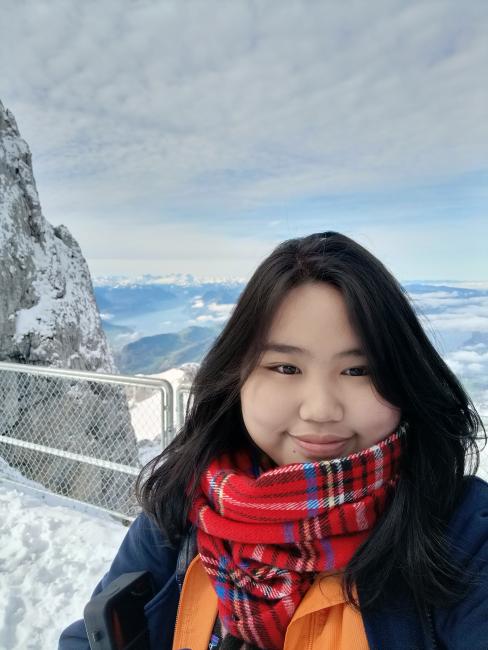 A Filipino college scholar bundled up in winter clothes in the foreground. Behind her is a view from snowy mountains.